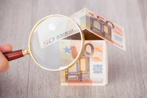Fingers holding magnifying glass to analyze house made of euro notes on table © apops - Fotolia.com