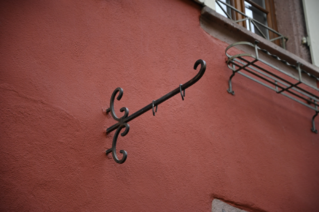 Antique handcrafted cast iron shutter dog against a Venetian red stucco wall in Riquewihr, Alsace France.